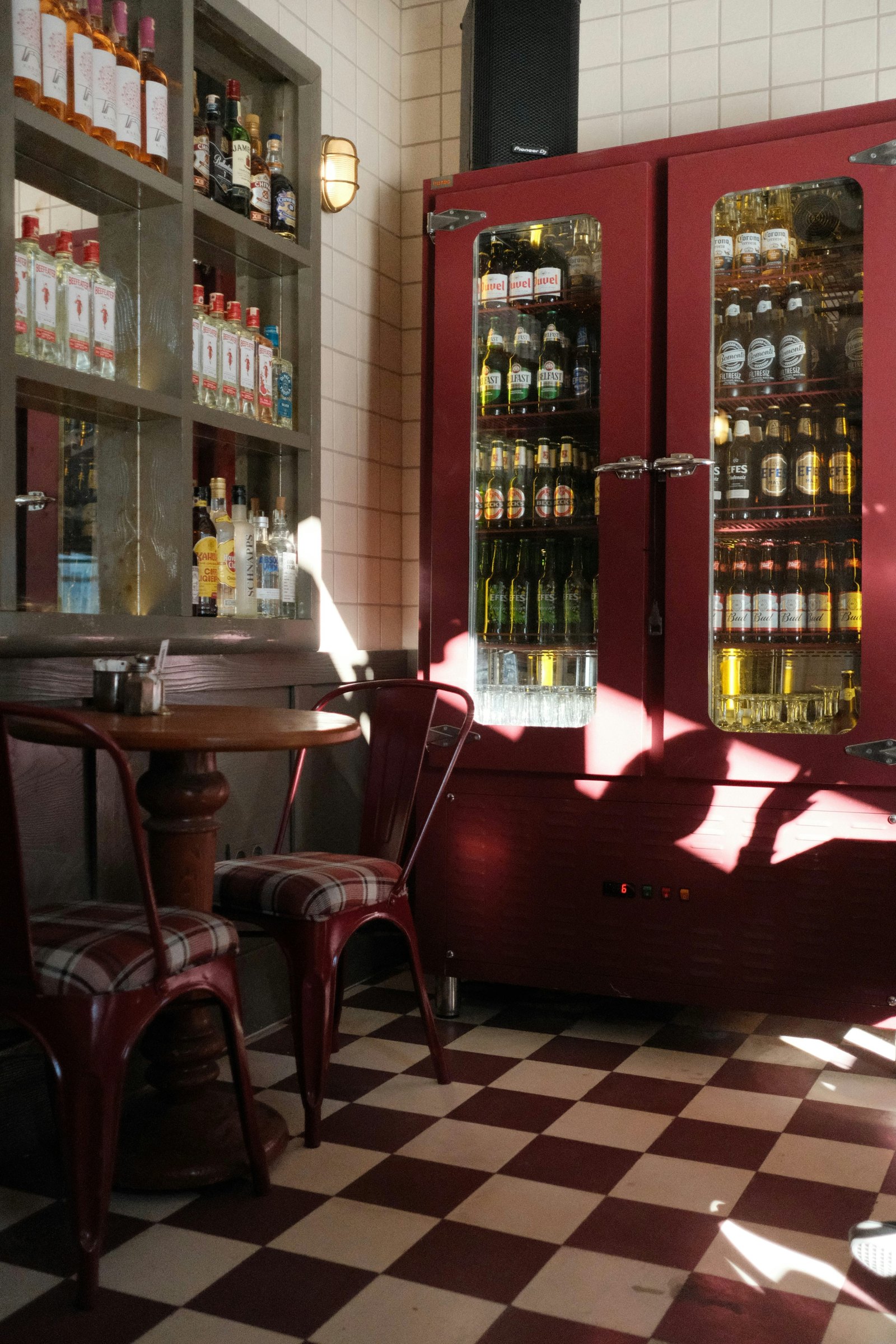 Sunlight falls across a small café table, red chairs and burgundy drinks cabinets in an empty bar